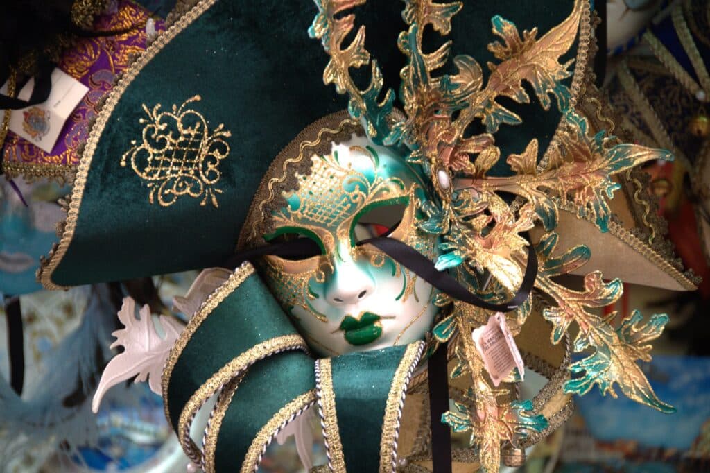 A Venetian mask for the Venice Carnival. This mask is mostly green, though is gold in parts. It is framed by a green hat and collar, but of which feature gold embroidery. The Venice Carnival is one of the best activities to do in Venice in January.