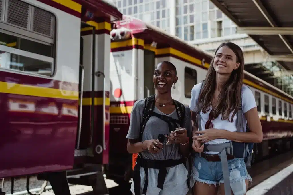 Ladies carry their  backpacks and smiling on a Railway Station Platform.
