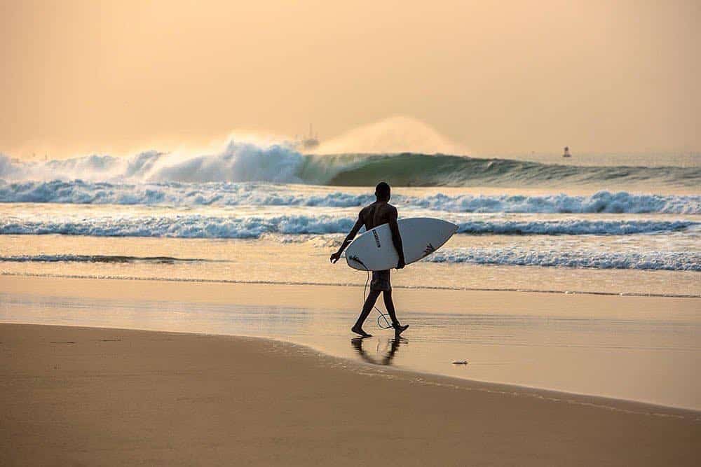 A lone surfer carrying his board, walking towards the sea at Tarkwa Bay Beach.